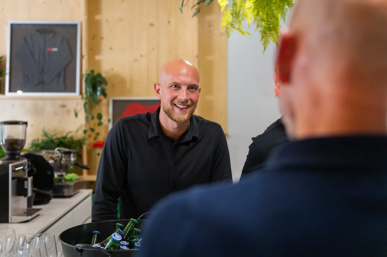 Een van de Borrelmeesters lacht naar een gast aan de bar