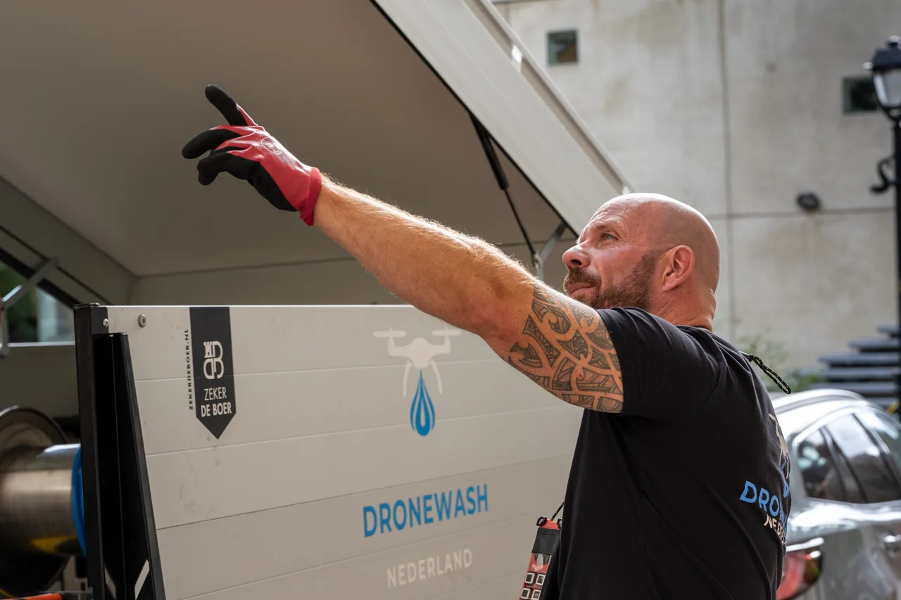 Een medewerker van DroneWash Nederland wijst naar de gevel, naast de bus