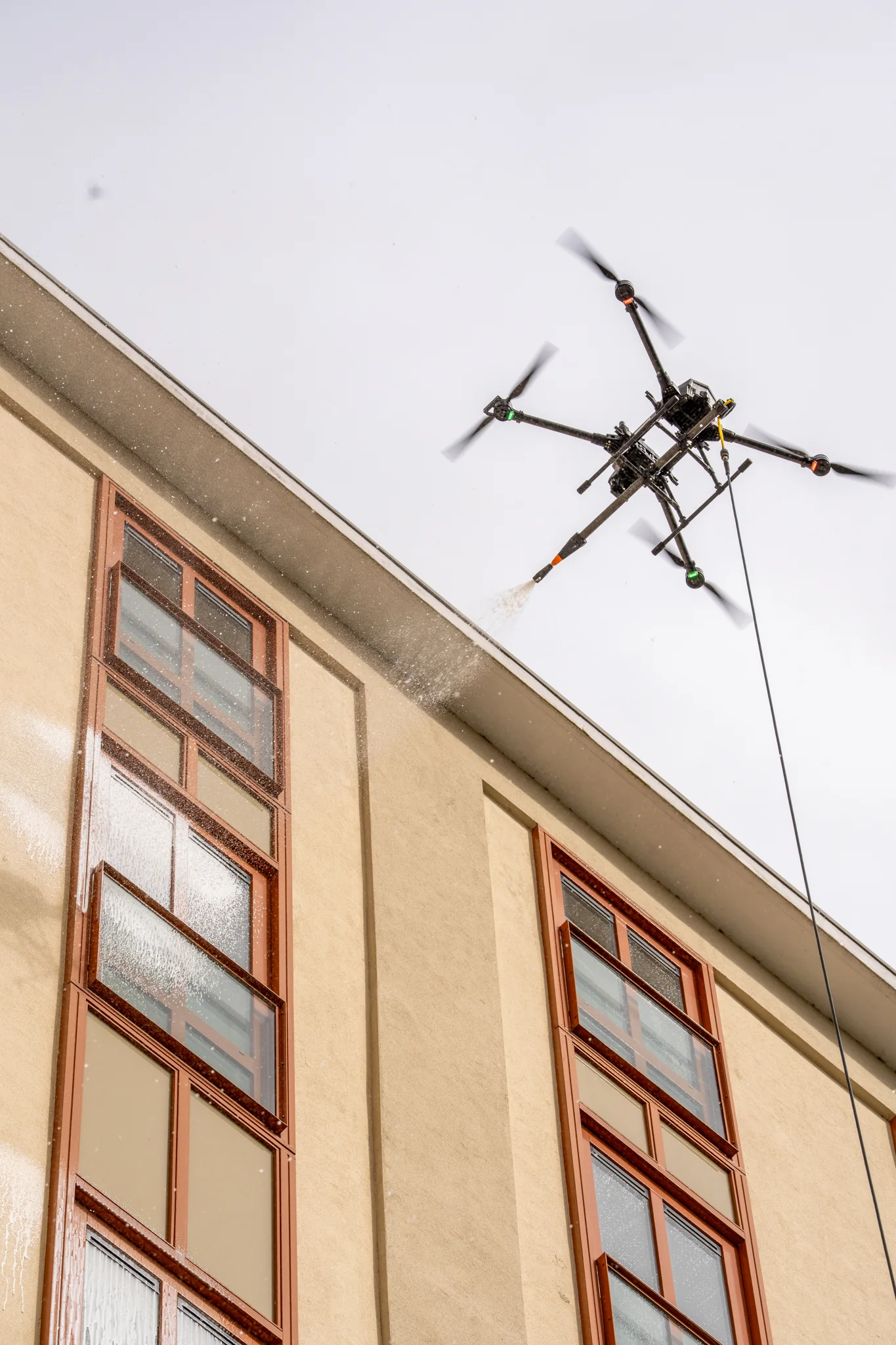 De drone spuit water tegen de gevel, vlak onder de dakrand